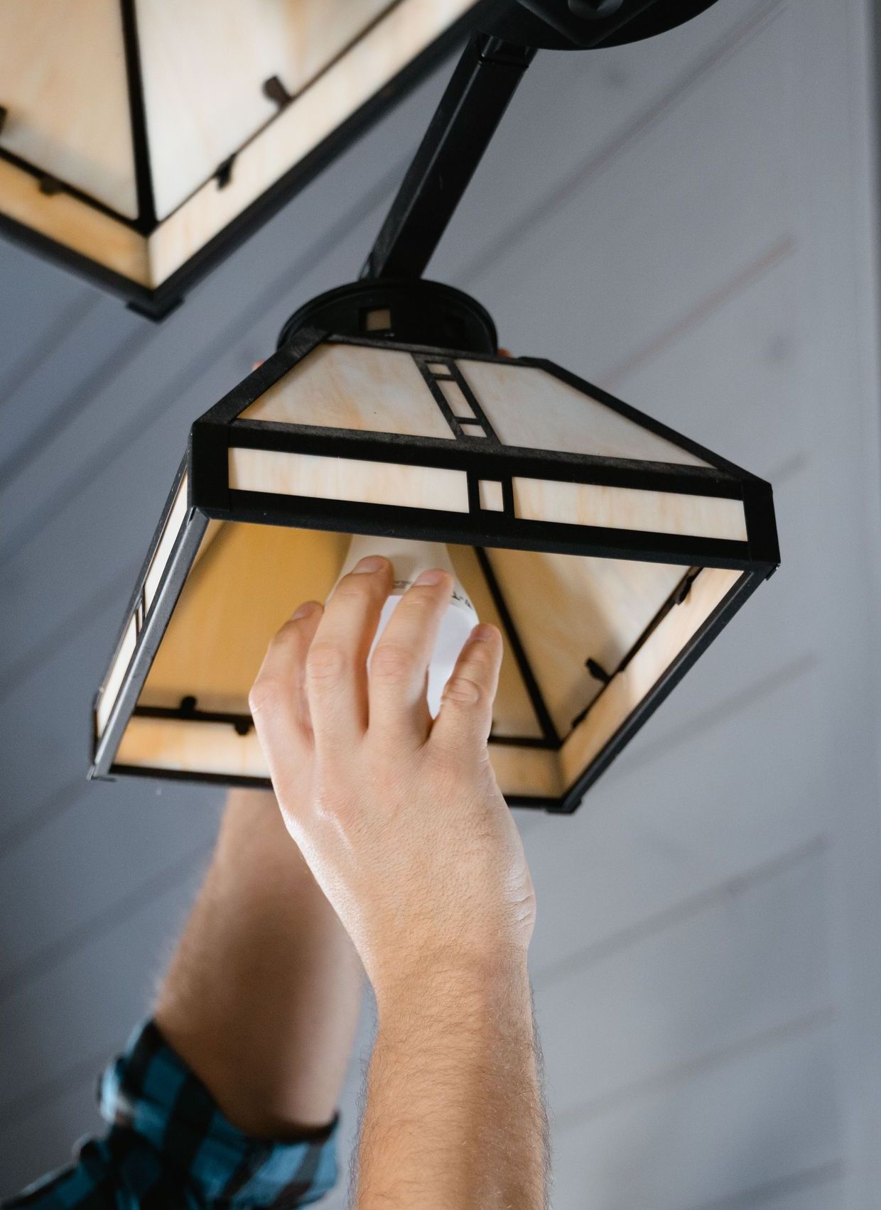 Man in plaid shirt fixing a pendant light indoors.