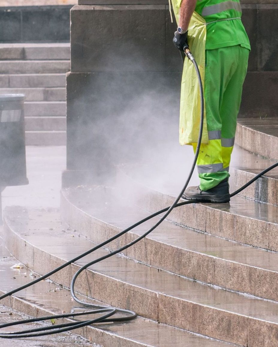A street worker pressure washes stone stairs in a public park, ensuring cleanliness and safety.